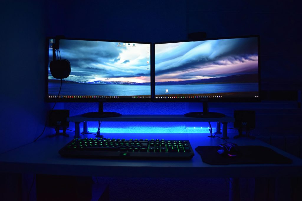 Dual monitors with blue lighting on a gaming desk setup.